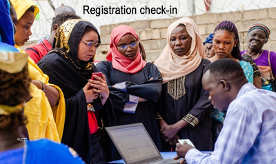 Registration Check in. A group of women huddle around a man bent over a computer typing.